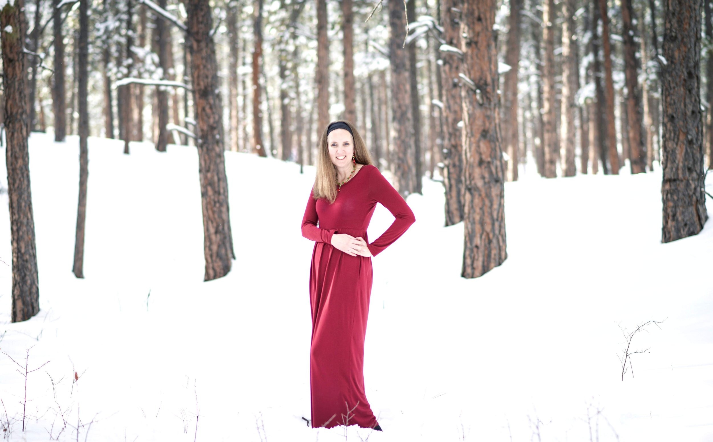 A woman in a red coat standing against the hush of winter snow, a bold flame of colour.