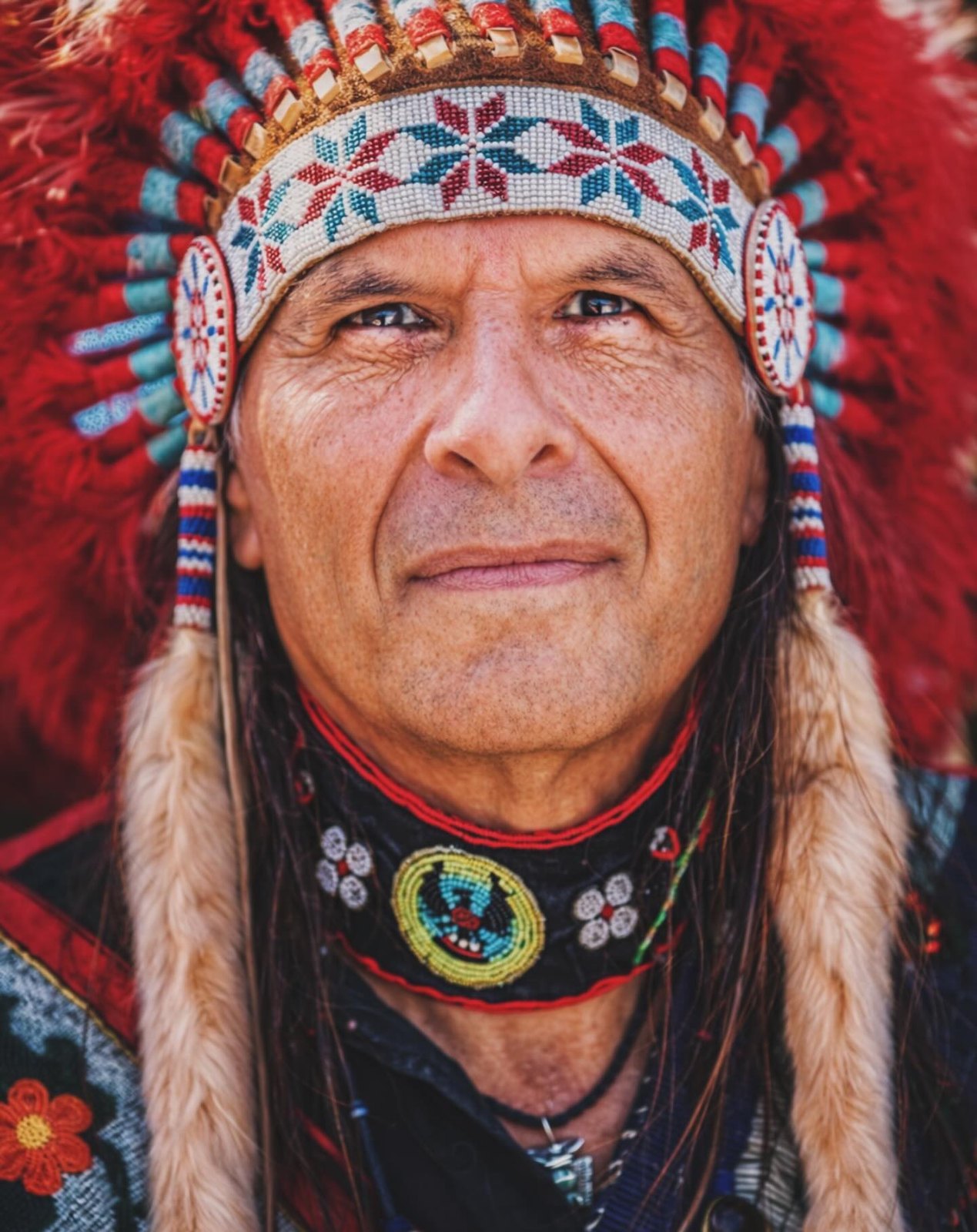 Formal portrait of a powwow chief in full regalia, feather headdress and beadwork rendered in fine detail.