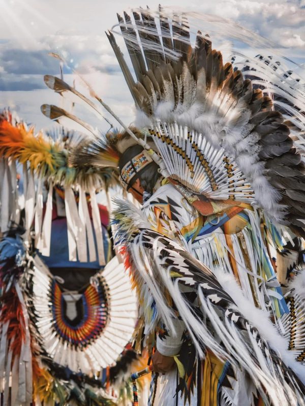 Close detail of powwow regalia — beadwork, feathers and fringe in rich colour.