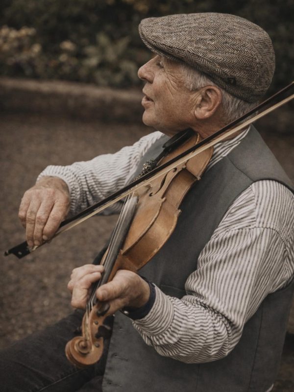 A street fiddler playing on an Irish street, talking with a passerby as he plays.
