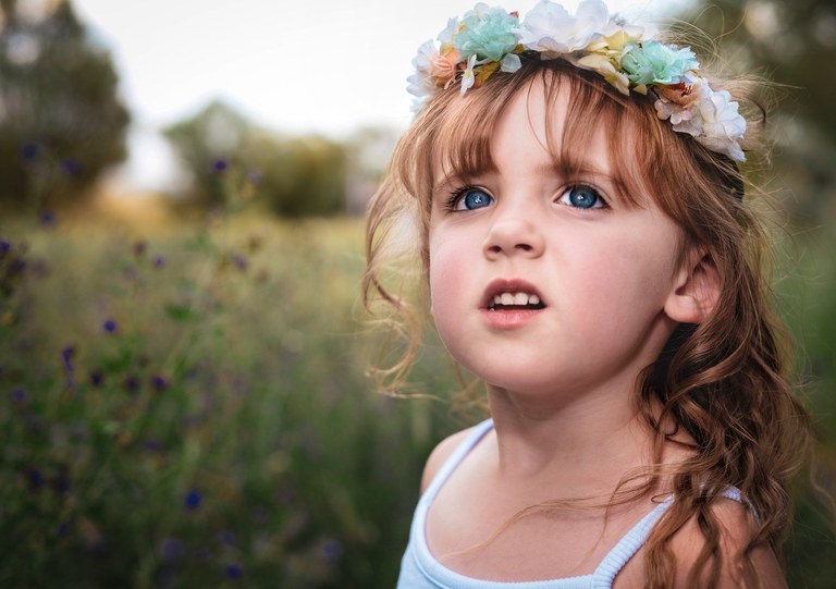 A young girl in a flowing gown wandering through wild flowers in warm golden light.